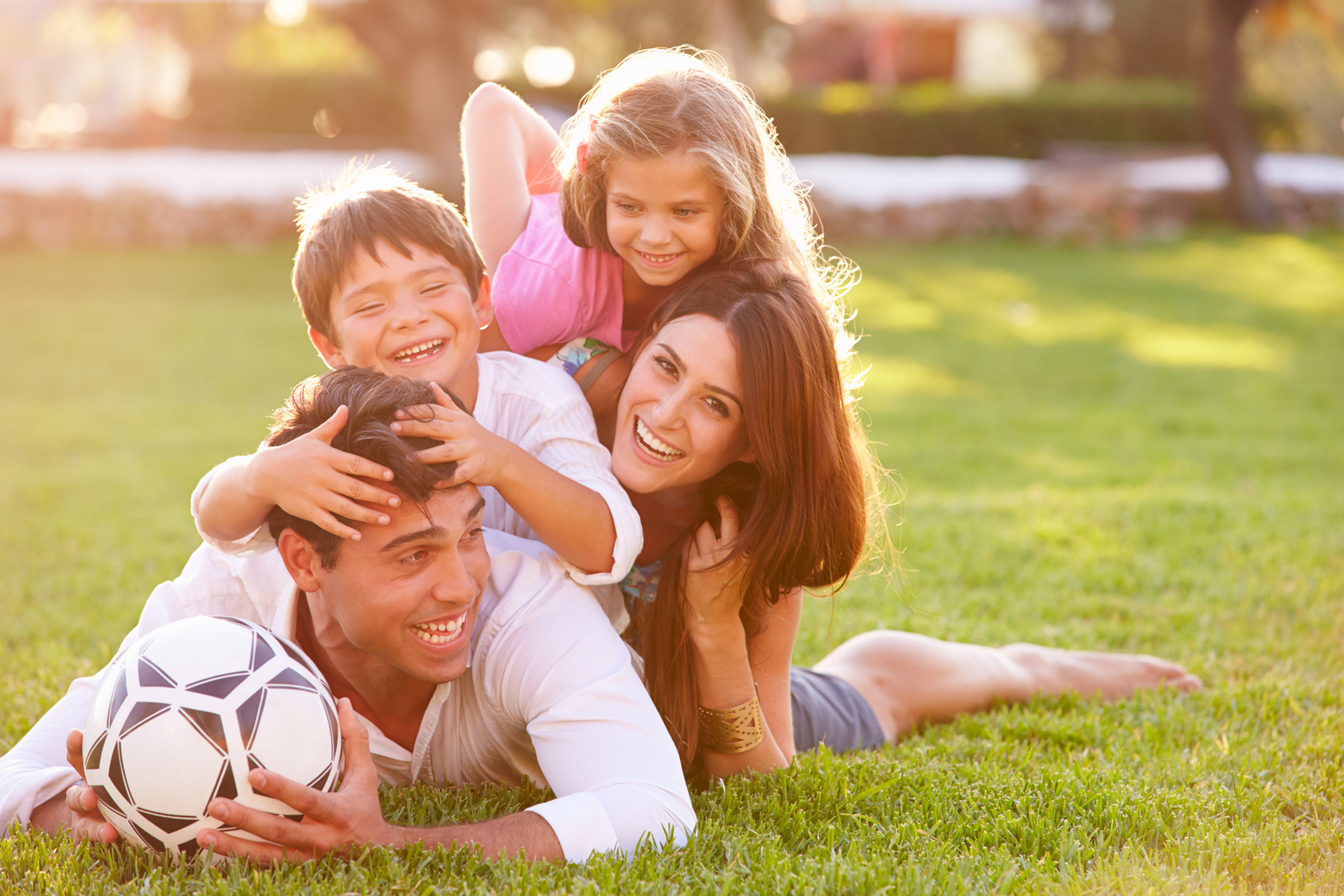 Family Lying In Pile Up On Grass Together